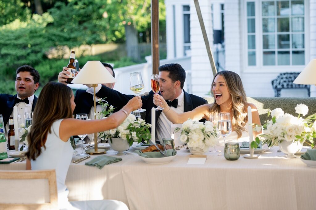 a wedding catering Paramount Events did in chicago this summer. Guests toast sitting outside by a long, white table with flower arrangements and entrees in front of them.